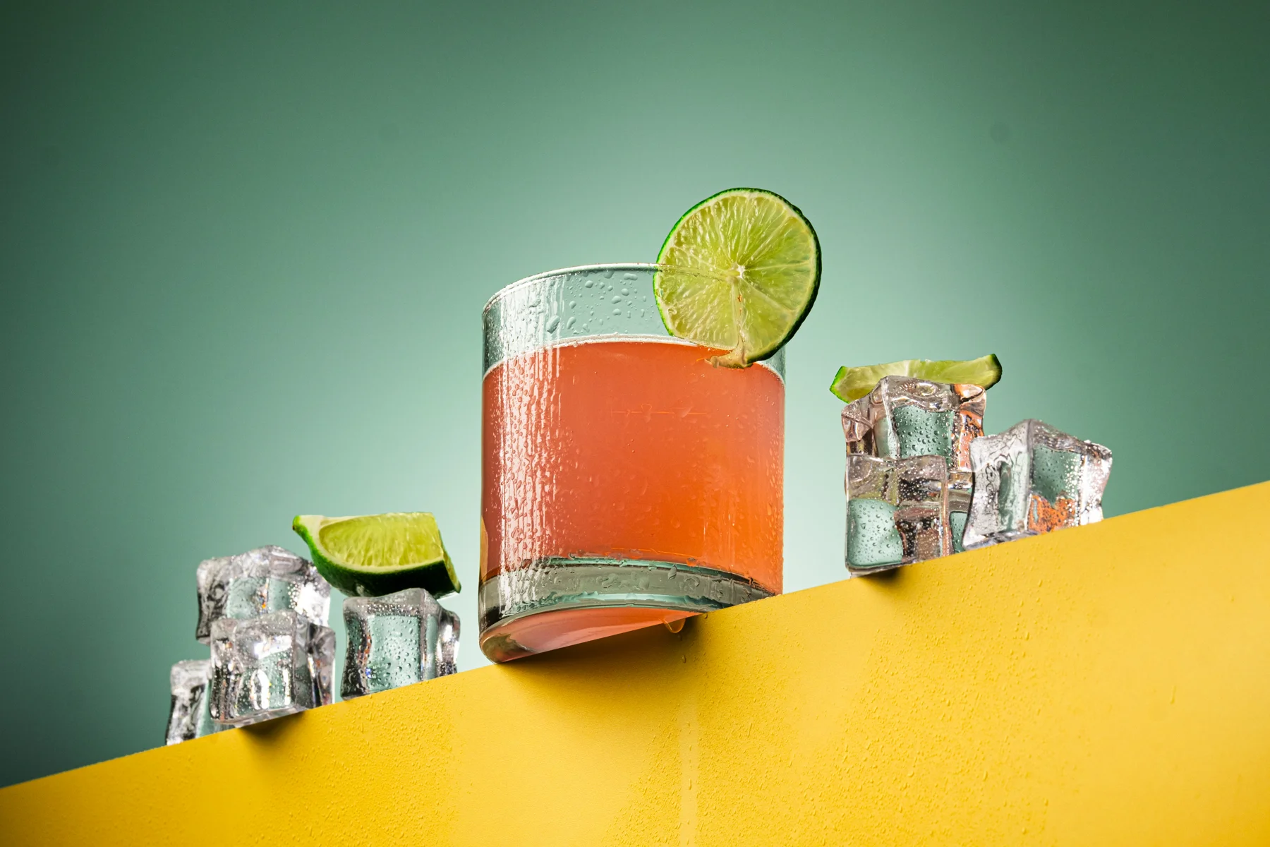 Pink citrus drink with lime and ice on a colourful set