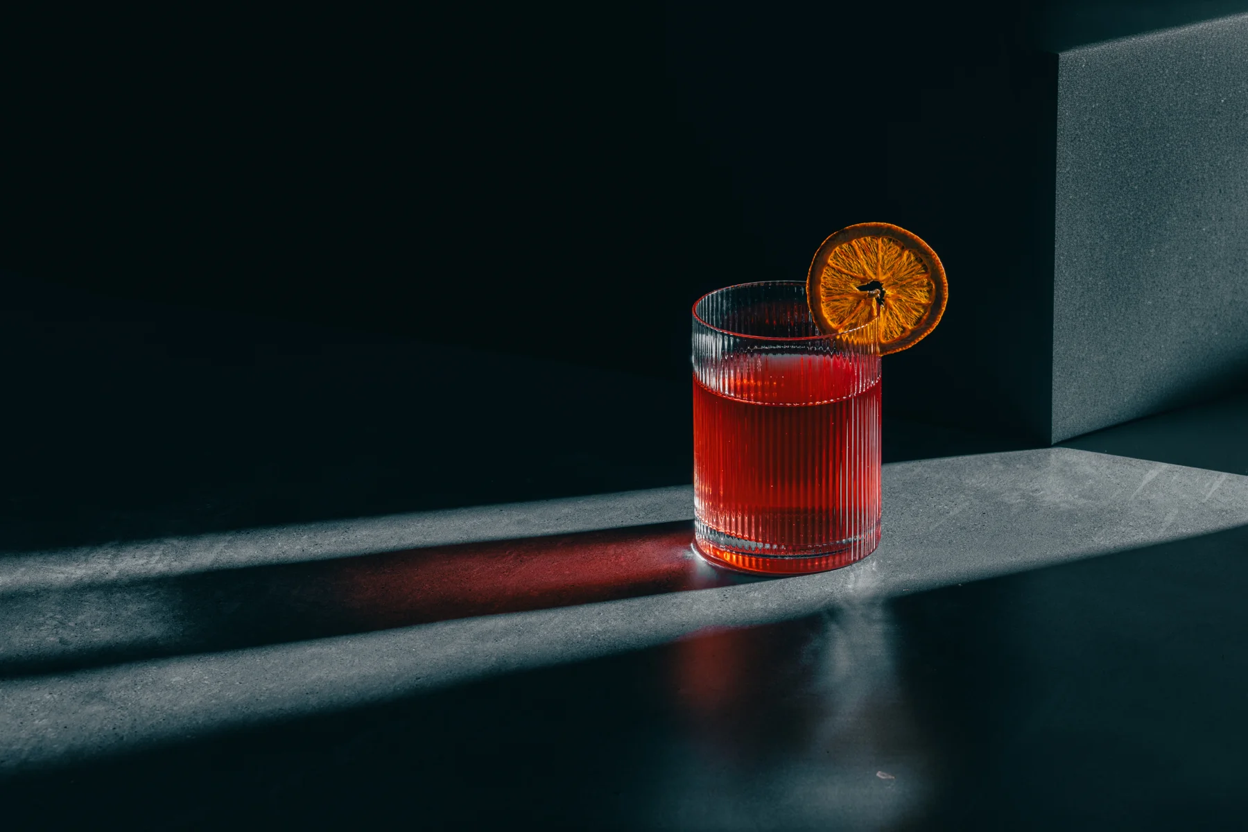 Red cocktail with an orange garnish in dramatic light